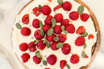 A sweet cake with white frosting an a lot of red raspberries and green garnish on top