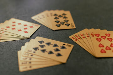 A royal flush out of hearts, cubs, spades and diamonds on gold colored cards on a gray table