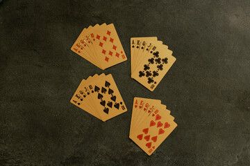 A royal flush out of hearts, cubs, spades and diamonds on gold colored cards on a gray table