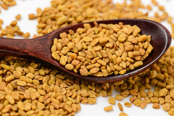A lot of scattered fenugreek seeds or shambhala with brown wooden spoon,  helba seeds macro photo