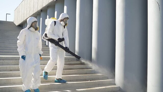 Two professional disinfectants in suits work together, protect humanity from covid, carry out sanitary treatment of the territory.