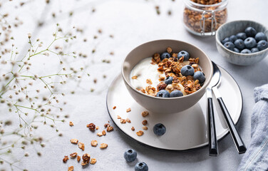 The concept of a healthy breakfast of yogurt, granola and fresh blueberry on a light background with flowers. Homemade diet and protein food.