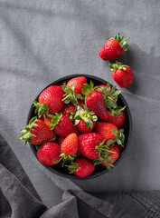 Juicy strawberries in a black bowl on a dark background with napkin. Farm ripe healthy berries. Top view