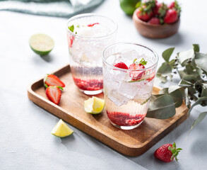 Fresh strawberry mojito in a glass with berries, lime, mint and ice in a wooden plate  on a light background. The concept of a summer refreshing drink for a party. Copy space.