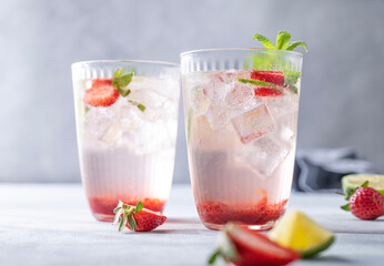 Fresh strawberry mojito in a glass with berries, lime, mint and ice on a light background with shadow. The concept of a summer refreshing drink for a party.