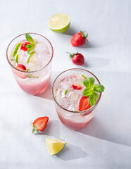 Fresh strawberry mojito in a glass with berries, lime, mint and ice on a light background with shadow. The concept of a summer refreshing drink for a party.