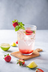 Fresh strawberry mojito in a glass with berries, lime, mint and ice on a light background with shadow. The concept of a summer refreshing drink.