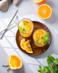 Freshly squeezed juice in a glass with fresh oranges, mint and ice on a light background with metallic tube and shadow. Healthy citrus detox drink for breakfast.