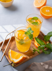 Freshly squeezed juice in a glass with fresh oranges, mint and ice on a light background with metallic tube and shadow. Healthy citrus detox drink for breakfast.