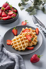 Homemade soft waffles with fresh strawberries in a plate on a light background. Traditional Belgian waffles. Healthy vegetarian breakfast