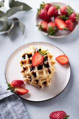 Homemade soft waffles with fresh strawberries and chocolate topping in a stack in a plate on a light background close up. Traditional Belgian waffles. Healthy  breakfast.