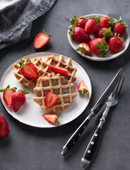 Homemade soft waffles with fresh strawberries and powdered sugar in a plate on a dark background. Traditional Belgian waffles.
