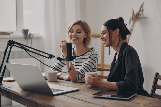 Two Attractive Young Women Talking And Smiling While Providing Live Stream In Studio Together