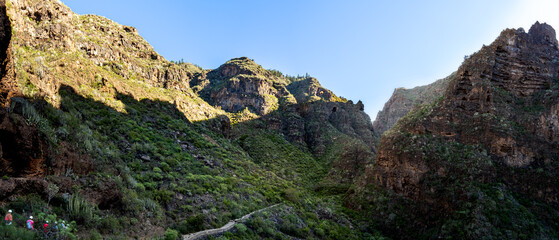 Hike through the tranquil and lush green nature along the cliffs of the Barranco del infierno ravine, Hell's gorge, in Adeje Tenerife with this panoramic view of tourists discovering the idyllic path.