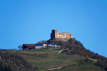 Fototapeta na wymiar Eine freistehende Burg auf einem Hügel in Südtirol mit einigen unterhalb liegenden Häusern, vor strahlend blauem Himmel