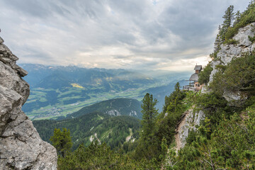 Fototapeta na wymiar View on a charming small mountain chapel built on the edge of a mountain cliff overlooking the valley in the austrian Alps on Stoderzinken mountain. Dachstein mountains.