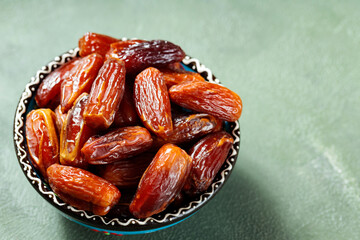 Pitted sweet dates on a green background. Bowl of dried dates for Ramadan. Copy space. Top view