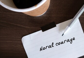 Coffee cup and pen writing words MORAL COURAGE, means courage to take action for moral reasons or...