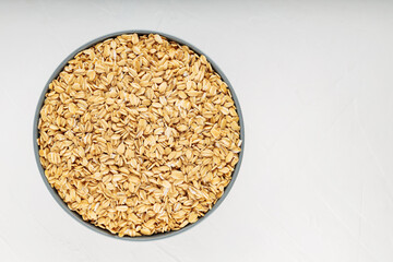Oat flakes bowl on a white background. Raw oatmeal for a healthy breakfast. Copy space. Top view