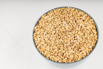 Oat flakes bowl on a white background. Raw oatmeal for a healthy breakfast. Copy space. Top view