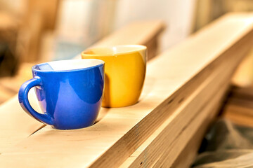 Work break, tea coffee time. Blue and yellow cups in carpentry on wooden planks