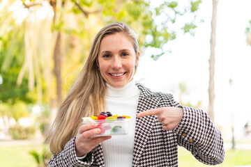 Young blonde woman holding a bowl of fruit at outdoors