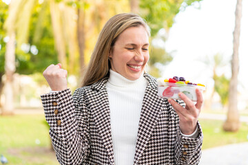 Young blonde woman holding a three dimensional puzzle cube at outdoors celebrating a victory