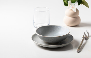 Table setting. Ceramic bowl and plate, silver cutlery, water and galss , on white table background.