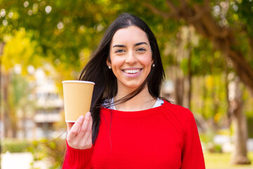 Young woman holding a take away coffee at outdoors smiling a lot
