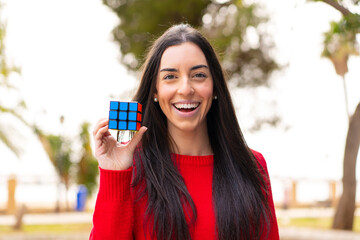 Young woman holding a three dimensional puzzle cube at outdoors with surprise and shocked facial...
