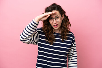 Young caucasian woman isolated on pink background looking far away with hand to look something