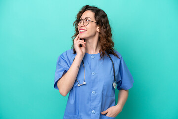 Young nurse caucasian woman isolated on blue background thinking an idea while looking up