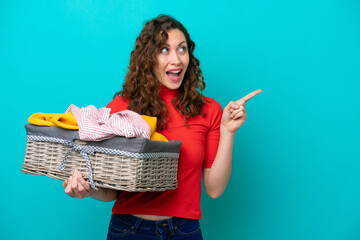 Young caucasian woman holding a clothes basket isolated on blue background intending to realizes...