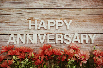 Happy Anniversary alphabet letters with flowers frame on wooden background