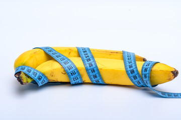 Żółte banany ze skórką owinięte niebieską metrówką krawiecką na jasnym tle - obrazy, fototapety, plakaty