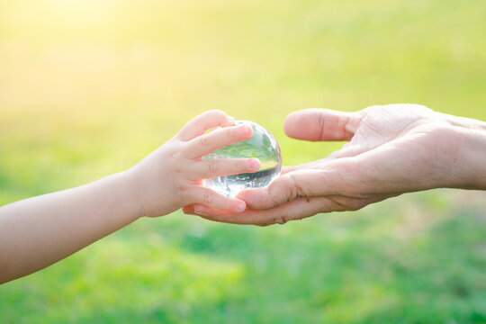 Adult person passes crystal ball to baby hand a healthy ecology to a new generation. Healthy ecology of the planet Earth. A healthy future for our generation. green glass background. Save the world.