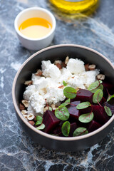 Bowl with beetroot and feta cheese salad, vertical shot on a black marble background, selective focus