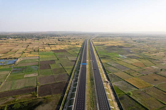 orbit aerial drone shot of new delhi mumbai jaipur express elevated highway showing six lane road with green feilds with rectangular farms