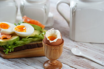 Soft-boiled egg in wooden egg cup    with toast eggs, salmon, avocado on the background.