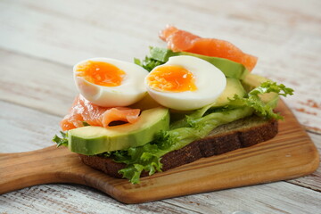 Avocado toast with egg, salmon, lettuce on the cutting board.