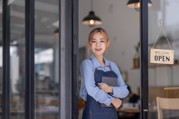 Portrait of Asian attractive small business owner standing in her shop entrance open sign, Portrait of asian tan woman barista cafe owner. SME entrepreneur seller business concept
