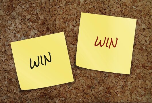 Two yellow notes on cork board with handwritten text WIN WIN, means a situation which each party benefits in some way, good for everyone that is involved