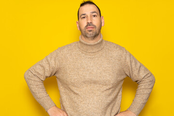 Cheerful bearded man wearing a red sweater posing isolated on gray background, studio portrait. People lifestyle concept. Mock up copy space. Standing with arms akimbo on waist blinking