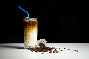 Glass of ice coffee latte with coffee beans on white table. Cold beverage in summer.