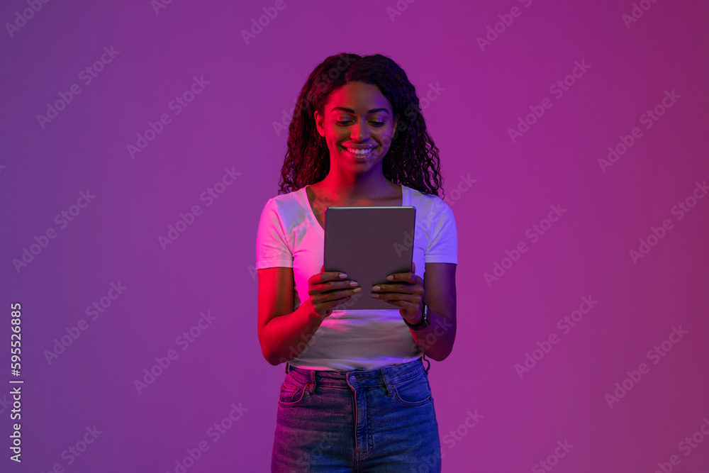 Aufkleber smiling black woman using digital tablet while standing in neon light