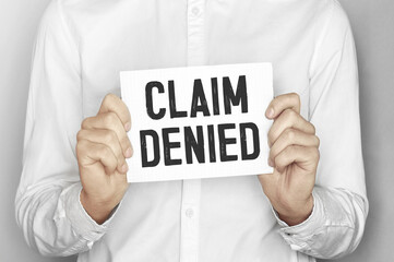 Man holding a paper card with text CLAIM DENIED