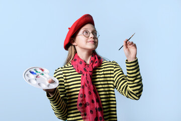 Fototapeta premium Girl with a palette of colors in a bright red beret and with a brush on a light blue background. Young artist