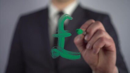 A businessman draws the Pound Sterling symbol on the glass. A man in a suit draws on glass with a brush and green paint.