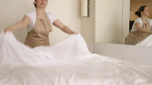 making bed, chambermaid in bedroom straightens bed linen, hotel room service