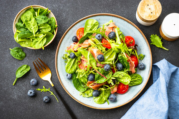Green salad with fresh prosciutto, green leaves mix and tomatoes at dark table. Flat lay.